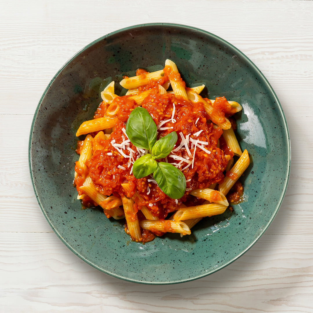 Teller mit MangiaMarc Tomatensoße mit Basilikum und Penne, bestreut mit frischem Parmesan, eine klassische italienische Pasta-Mahlzeit.