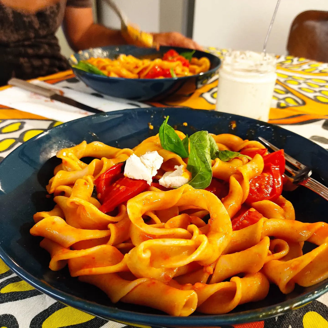 Ein Teller mit Sagne Incannulate, vermischt mit halbierten, leuchtend roten Cherry-Tomaten und cremigen Stücken Büffelmozzarella. Frische Basilikumblätter setzen grüne Akzente.