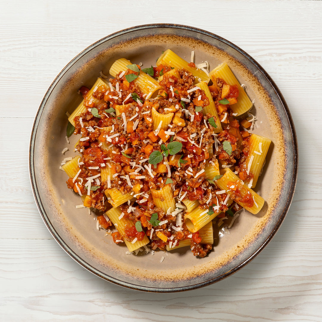 Teller mit MangiaMarc Premium Ragù Bolognese und Rigatoni, garniert mit frischem Basilikum, Nahaufnahme des fertigen italienischen Pasta-Gerichts.