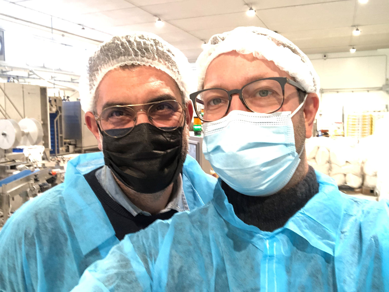 Zwei Männer in Hygieneschutzkleidung mit Haarnetz und Mundschutz in einer Lebensmittelproduktionshalle