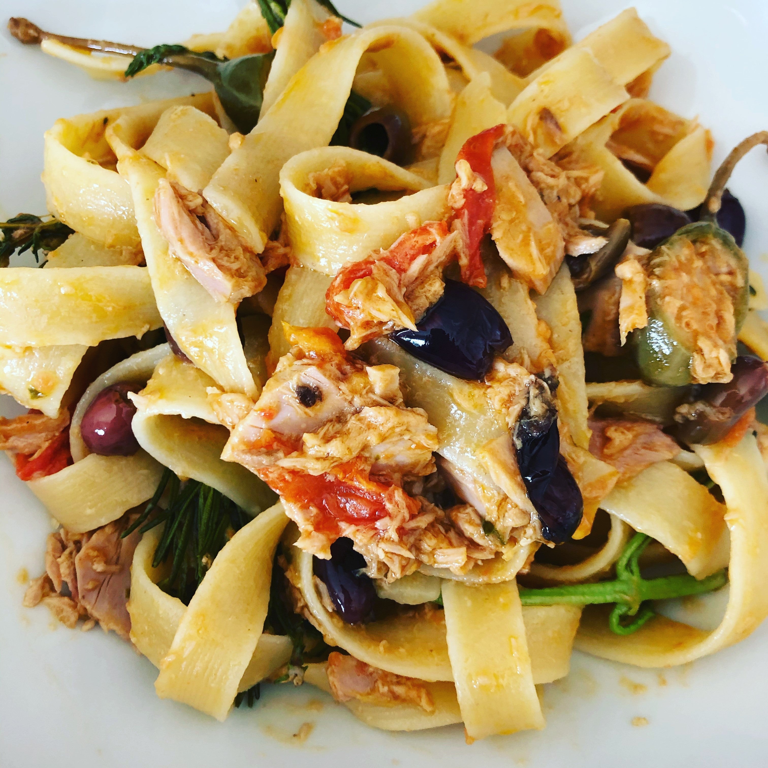 Tagliatelle mit Thunfisch, Tomaten, Oliven und Kapern auf weißem Teller