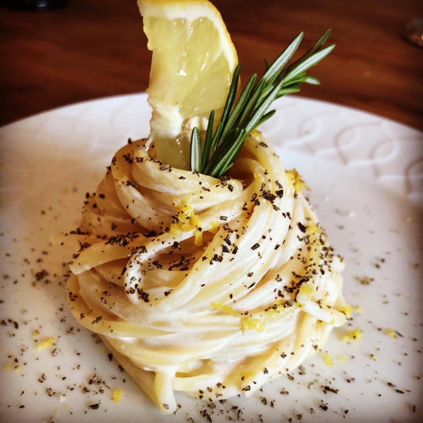 Spaghetti Cacio e Pepe als Nest angerichtet, garniert mit Zitronenspalte und Rosmarinzweig auf weißem Teller