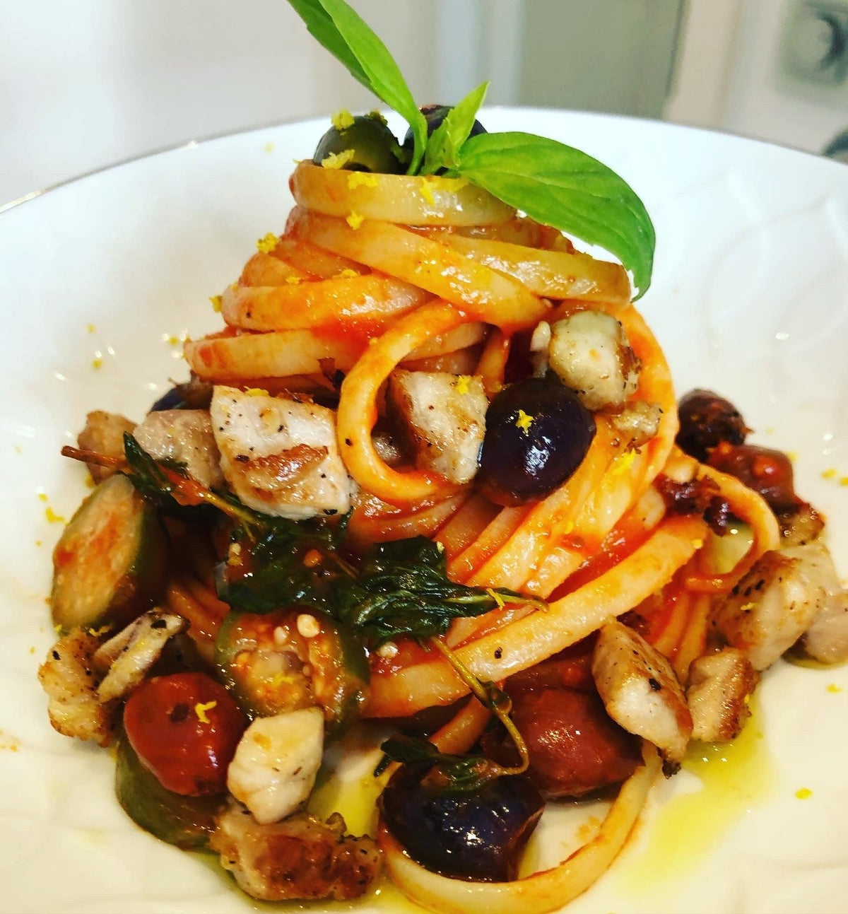 Tagliatelle mit Tomatensauce, Mozzarella-Würfeln und Oliven, als Türmchen angerichtet und mit Basilikum garniert auf weißem Teller