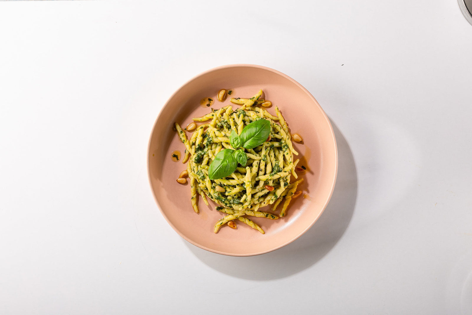 Trofie-Pasta mit grünem Pesto in rosafarbener Schale auf weißem Untergrund
